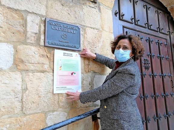 La directora de Cáritas, Sonsoles López, colocando un cartel en la entrada de la Catedral de Santander. / ALERTA