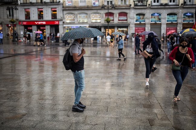 Archivo - Ciudadanos resguardándose de la lluvia durante una manifestación en la Puerta del Sol el pasado 5 de junio en Madrid