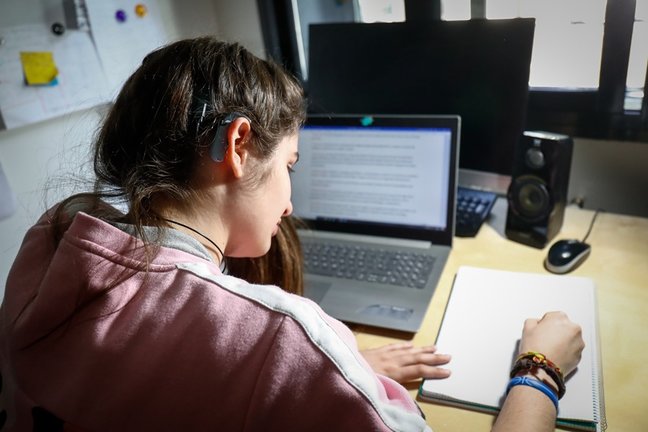 Archivo - Una joven usuaria de audífonos estudia en su habitación