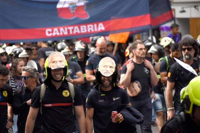 Bombero de Cantabria marchan junto a un cartel electoral del PSOE. / Richard Zubelzu