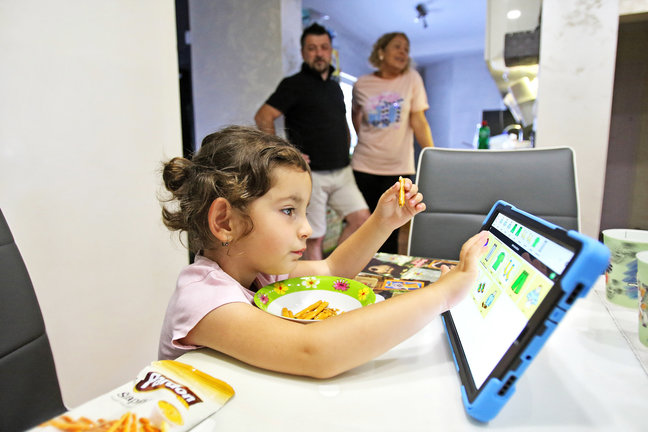 Una niña comiendo mientras juega con una tablet. / EP