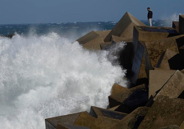 Una persona contempla de cerca las olas rompiendo en el rompeolas del espigón del puerto de Cudillero. EFE / Paco Paredes