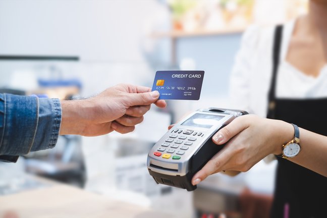 Una persona pagando con tarjeta de crédito en un datafono de un comercio. EP