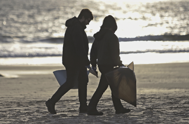 Dos personas durante la limpieza de pellets en una playa. / ALERTA