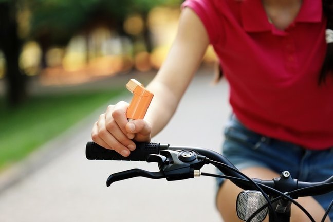 Una mujer montando en bici con un inhalador en su mano. / EP