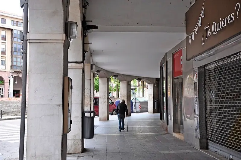Un hombre de avanzada edad camina bajo los soportales junto a la plaza Mayor de Torrelavega. / S.D.