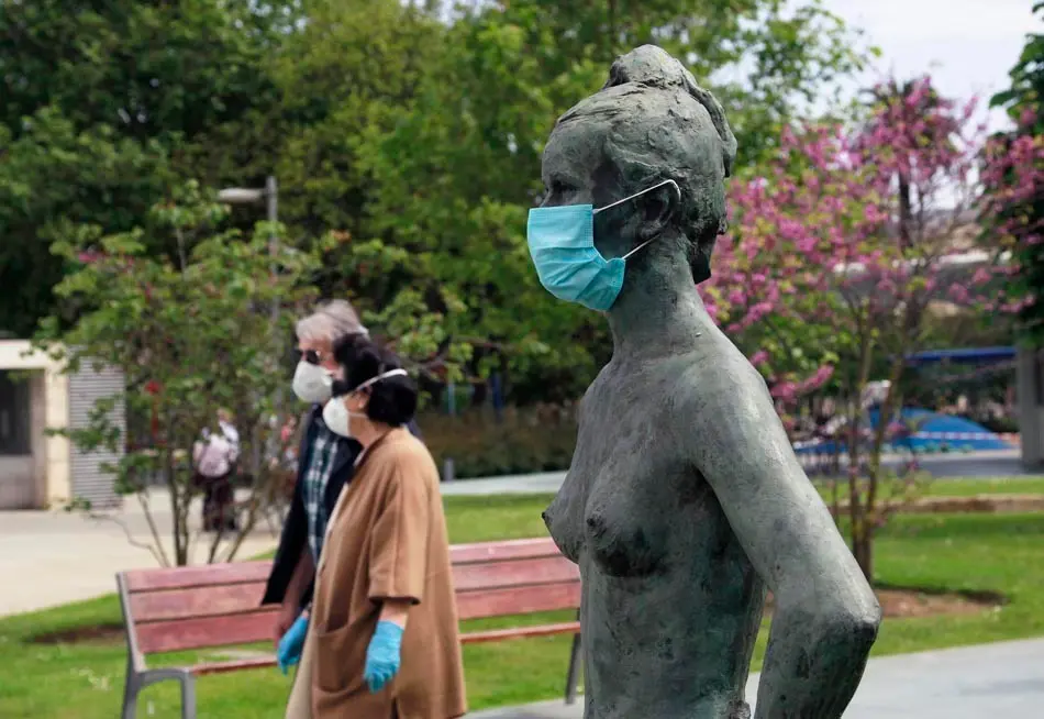 Varias personas con mascarilla caminan junto a una estatua en los jardines de Pereda cubierta tambi&eacute;n por mascarilla. / J. Ram&oacute;n
