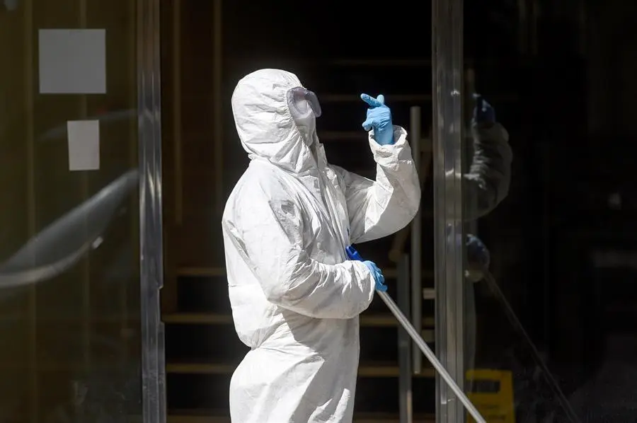 Un hombre desinfecta este martes el portal del edificio de Santander en la calle Nicol&aacute;s Salmer&oacute;n, donde los vecinos llevan m&aacute;s de diez d&iacute;as confinados en sus domicilios tras detectarse un brote de coronavirus en ese inmueble que afecta a 15 de sus 80 residentes y esperan la prueba PCR que les van a realizar hoy para conocer si en las pr&oacute;ximas horas pueden finalizar su cuarentena y salir ya de sus casas. EFE/Pedro Puente Hoyos