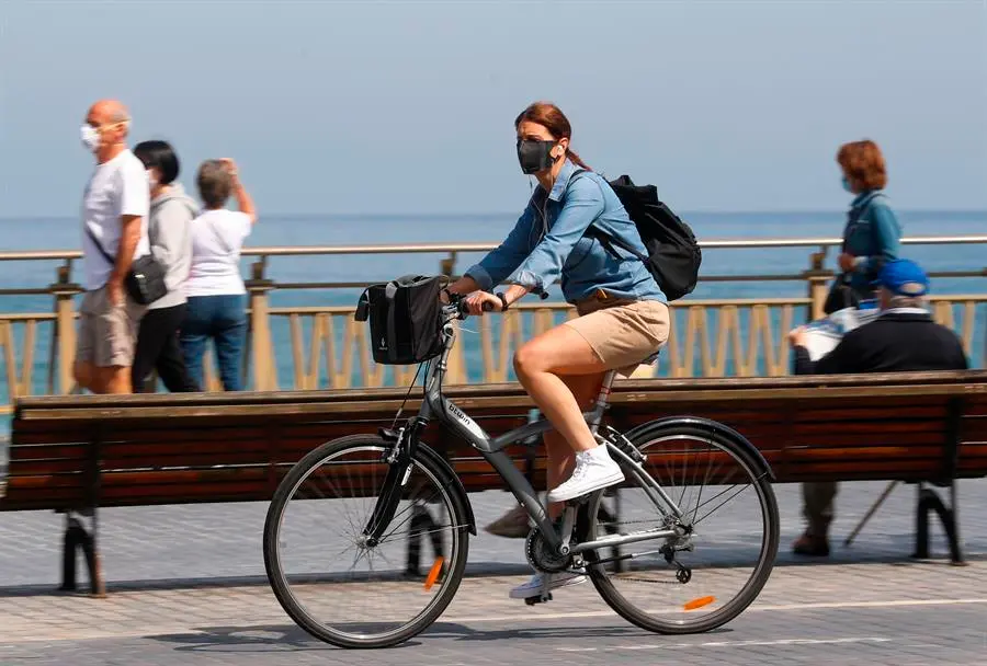 Una mujer pasea en bicicleta protegida con una mascarilla por el paseo de la Zurriola de San Sebasti&aacute;n. EFE/Juan Herrero/Archivo