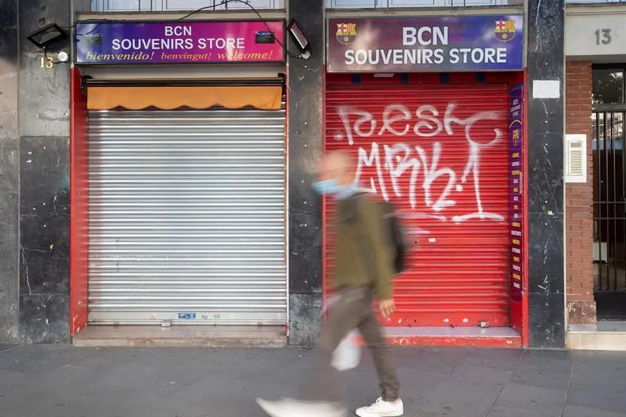 Un vecino pasa ante una tienda de recuerdos con la persiana bajada en un comercio cercano al Camp Nou. EFE/ Marta P&eacute;rez/Archivo
