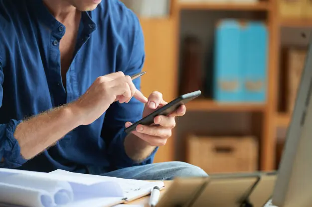 hombre-irreconocible-vestido-informalmente-usando-telefono-inteligente-trabajo-oficina_1098-20449