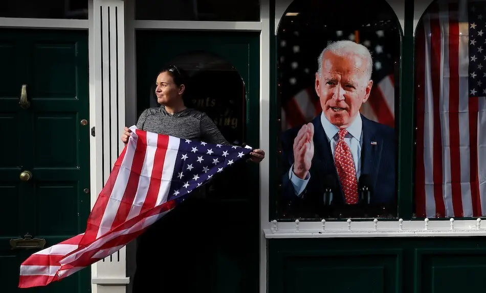 Catherine Hallahan, due&ntilde;a de los barberos de Hallihan, en Ballina sostiene la bandera nacional de los Estados Unidos mientras los residentes comienzan las celebraciones en el hogar ancestral del candidato presidencial estadounidense Joe Biden en anticipaci&oacute;n de los resultados de las elecciones estadounidenses mientras Biden se acerca a la victoria sobre Donald Trump. Foto: Brian Lawless / PA Wire / dpa