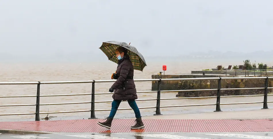 Una persona con su parag&uuml;as y mascarilla bajo la lluvia en Santander. / HARDY