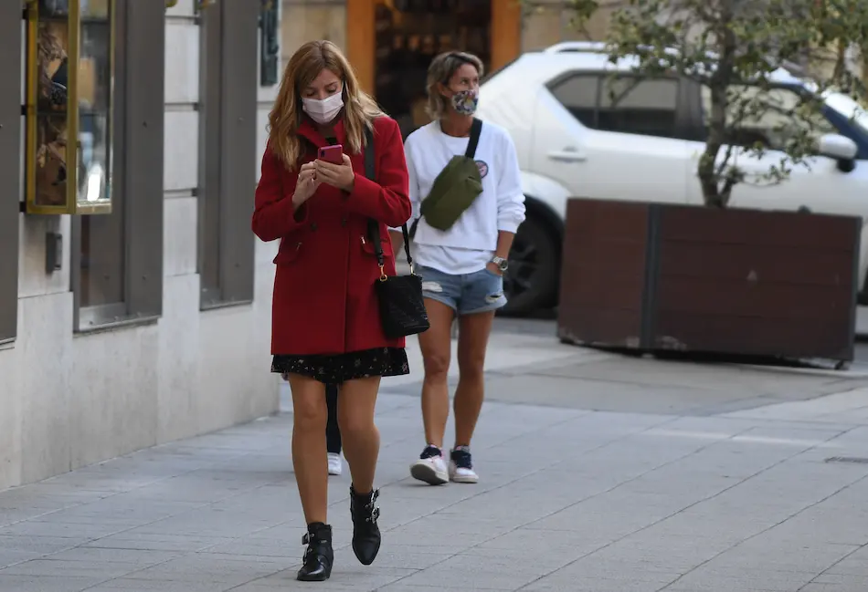 Una persona con su mascarilla observa su tel&eacute;fono m&oacute;vil en una calle del centro de Santander. / HARDY