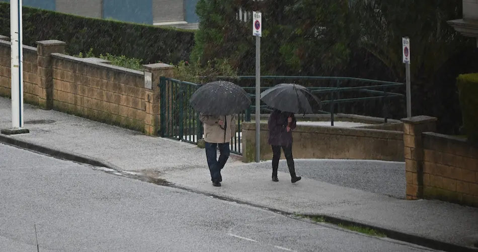 Varias personas caminan bajo una intensa granizada en la zona de Valdenoja, Santander. / HARDY