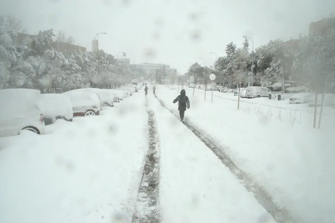 Algunas personas caminan por una calzada completamente cubierta de nieve de una calle en Alcobendas, Madrid (Espa&ntilde;a) a 9 de enero de 2021