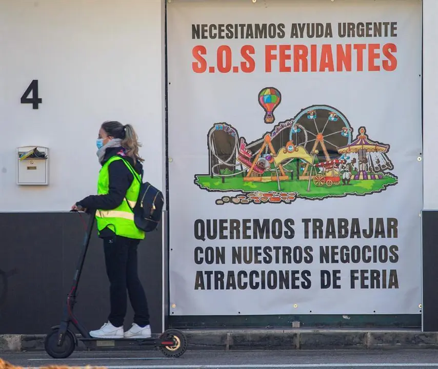 Una mujer pasa con un patinete el&eacute;ctrico por delante de un cartel que informa sobre la situaci&oacute;n de un sector empresarial afectado por la pandemia. EFE/ Cati Cladera