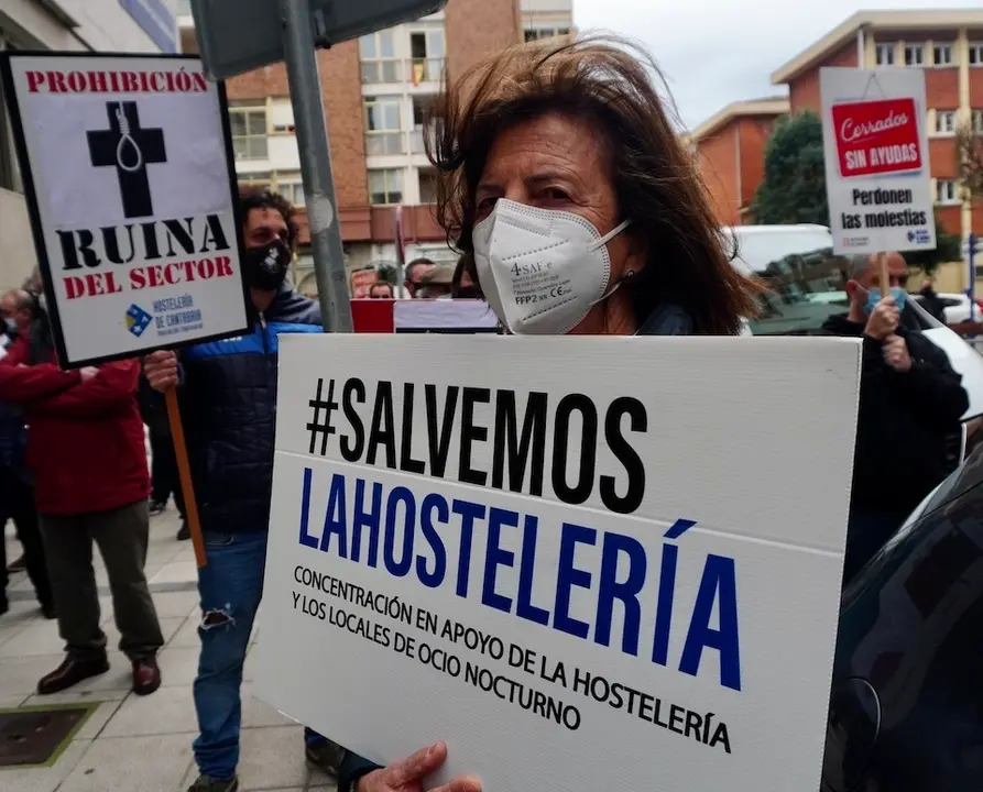 Una mujer sostiene un cartel en la manifestaci&oacute;n frente a la consejer&iacute;a de Sanidad para pedir la vuelta a la actividad de la hosteler&iacute;a. / HARDY