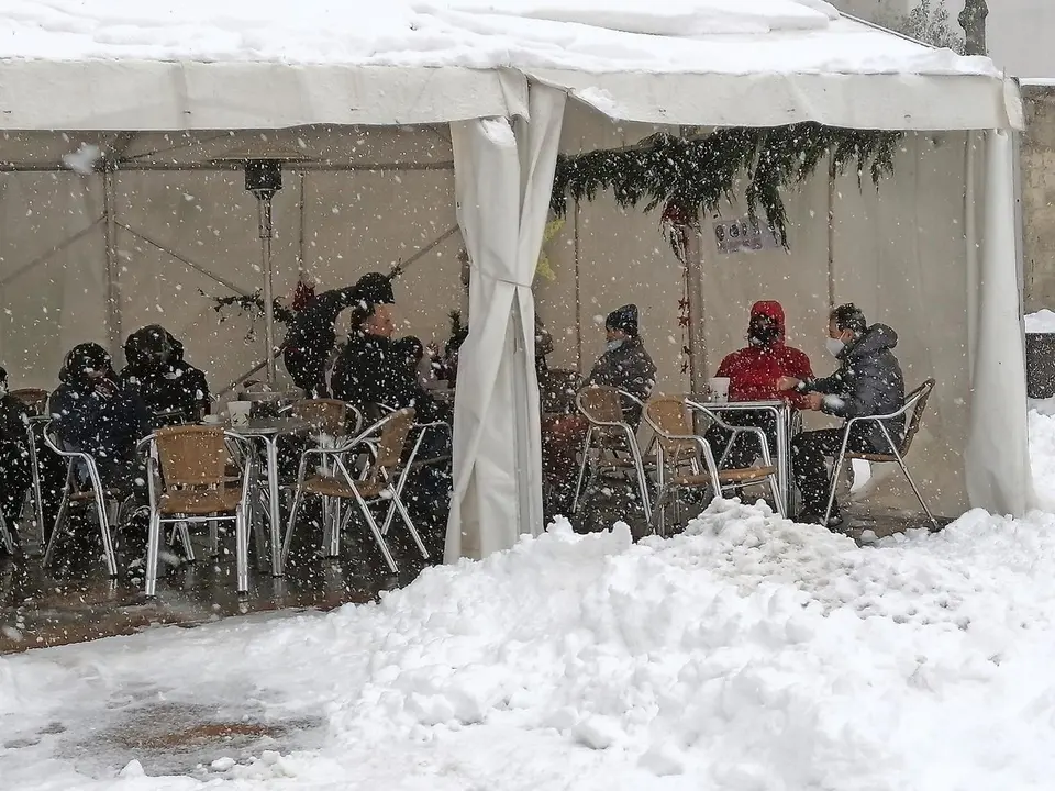 Varias personas en una terraza en la localidad de Reinosa donde la nieve cubre las principales calles. Foto: Queimadelos