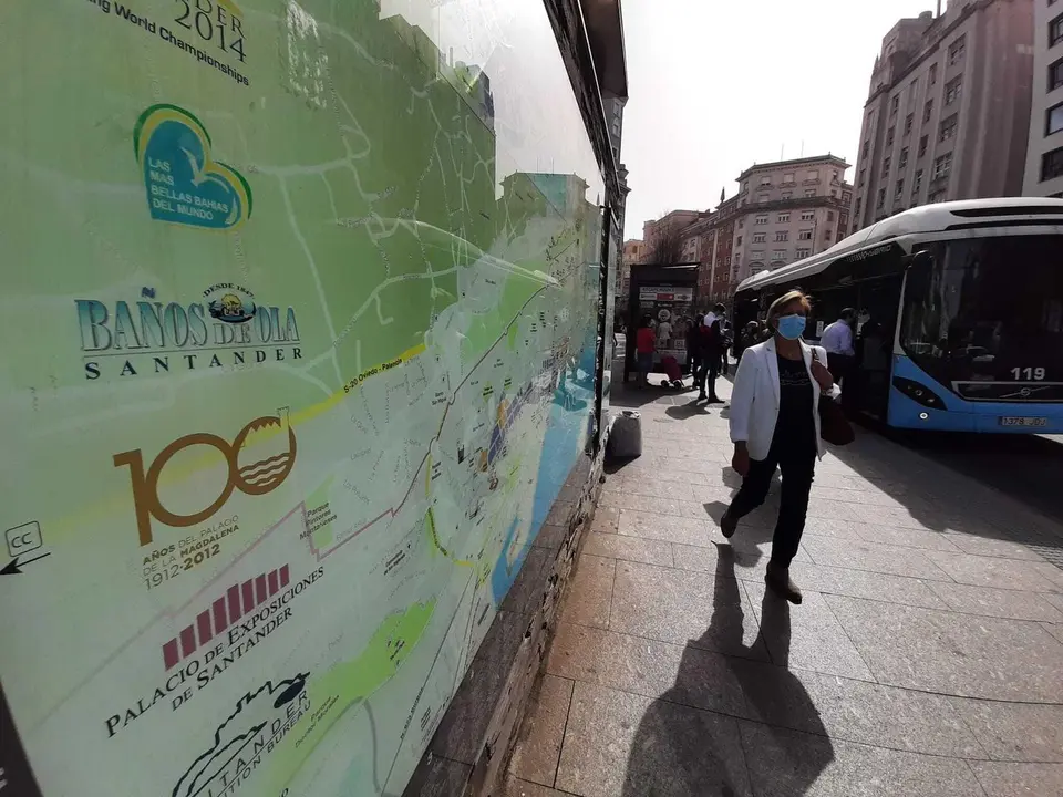 Una persona con mascarilla pasa delante de un cartel del Ayuntamiento donde se describe los puntos de inter&eacute;s tur&iacute;sticos. / S. D&iacute;az