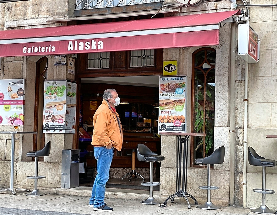 Una persona con mascarilla a la puerta de un establecimiento hostelero en el centro de Santander vac&iacute;o. / HARDY