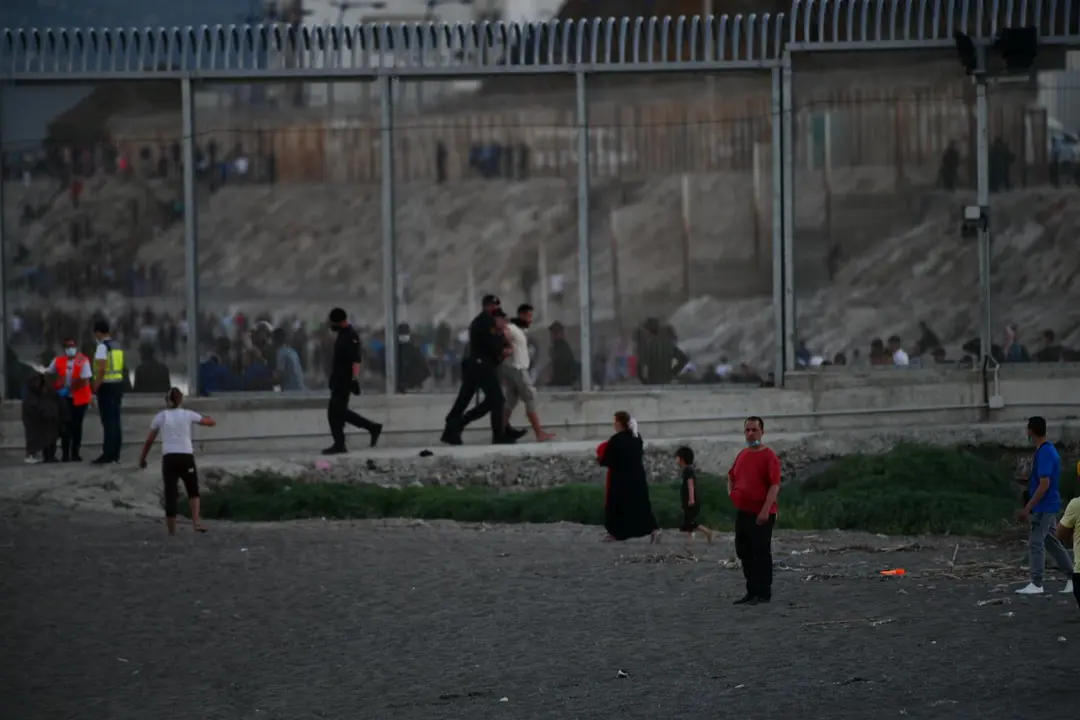 Agentes de Polic&iacute;a y personas migrantes en la playa del Tarajal
