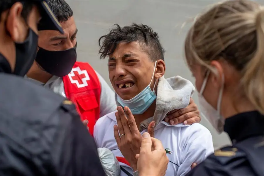 Un migrante que ten&iacute;a miedo de ser devuelto a Marruecos llora ante un voluntario de Cruz Roja y un efectivo de la Polic&iacute;a Nacional, hoy viernes en la nave de el pol&iacute;gono industrial cercano a la playa de El Tarajal en donde permanecen gran parte de los menores migrantes llegados a Ceuta. La frontera del Tarajal que separa Ceuta de Marruecos as&iacute; como el espig&oacute;n fronterizo no han registrado esta noche ni a primeras horas de la ma&ntilde;ana de este viernes intentos de entrada, de modo que no se cumplen ya dos d&iacute;as sin actividad en la zona. EFE/ Brais Lorenzo