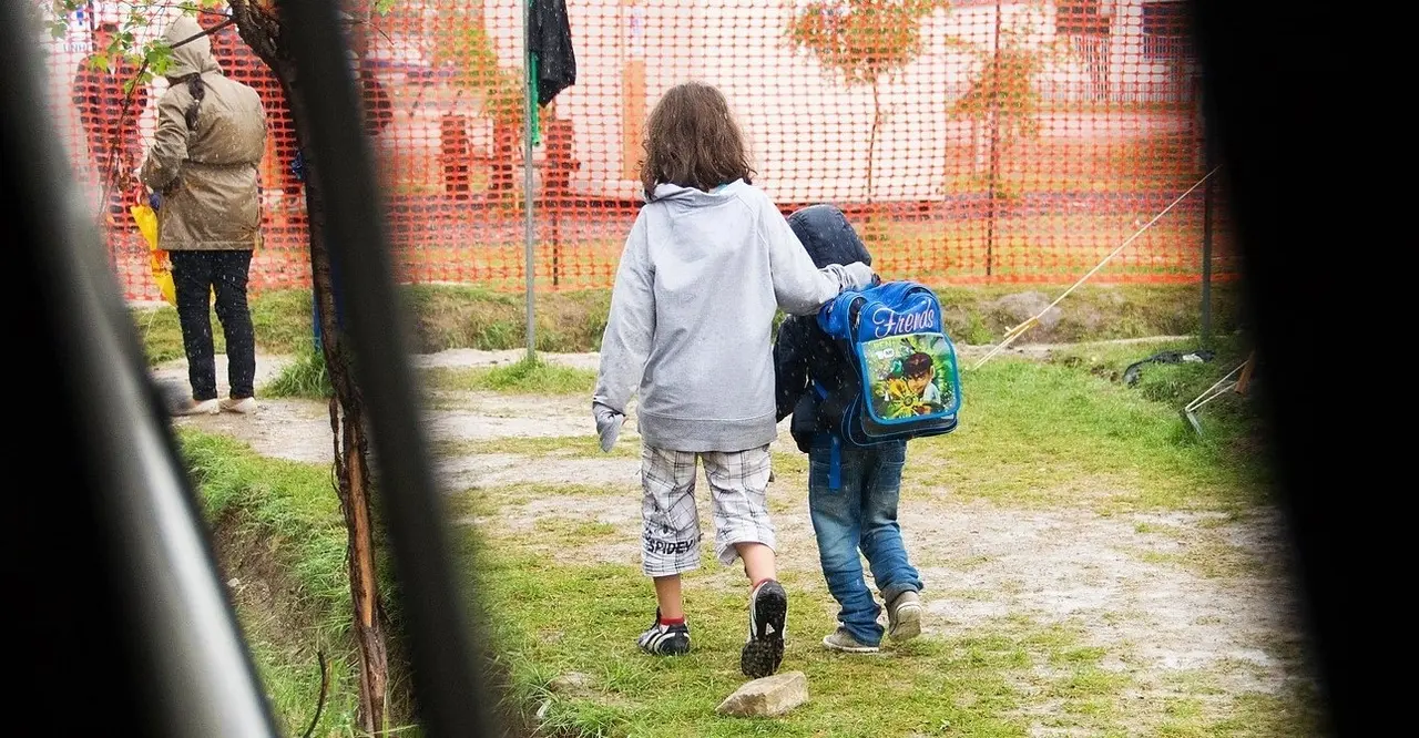 Dos ni&ntilde;os caminan bajo la lluvia en el entorno de un colegio