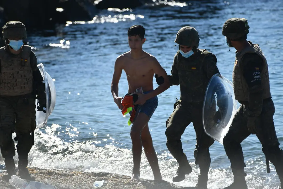 Dos militares del ej&eacute;rcito espa&ntilde;ol ayudan a un menor migrante procedente de Marruecos a su llegada a Ceuta