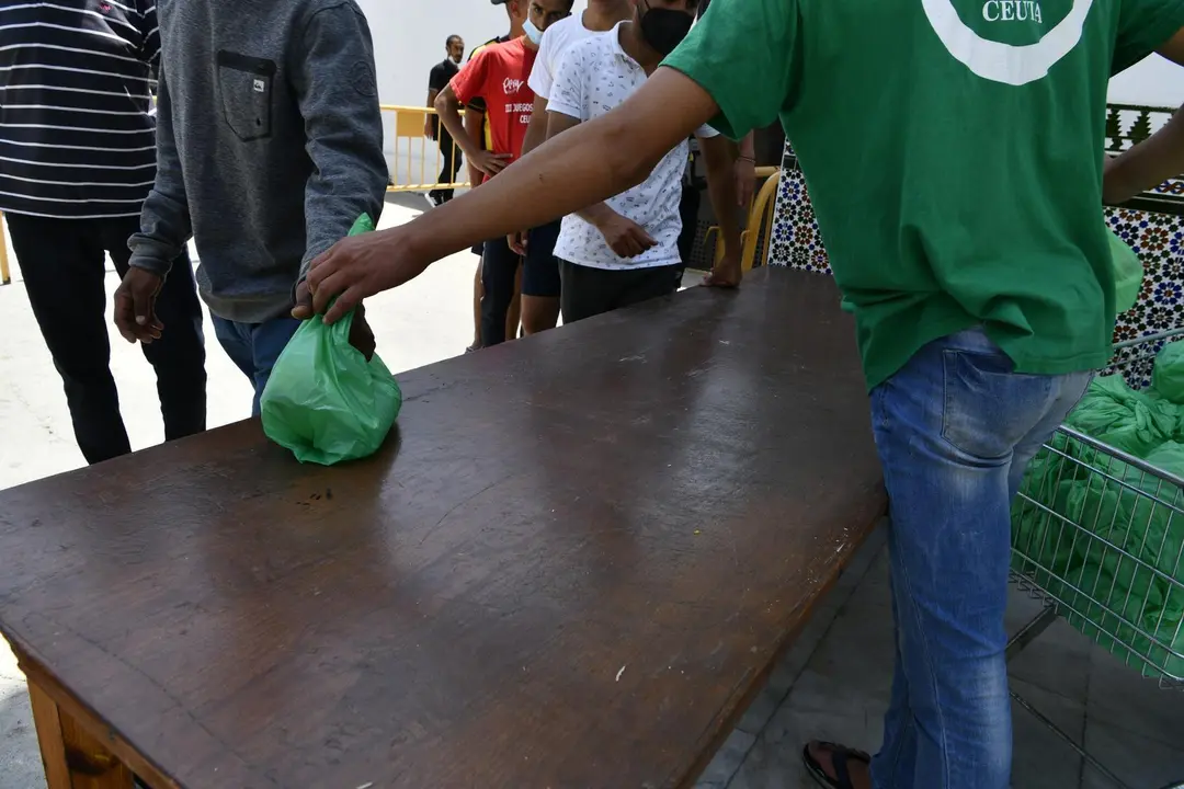 Un miembro de la asociaci&oacute;n isl&aacute;mica 'Luna Blanca' reparte una bolsa de comida a varios migrantes en Ceuta (Espa&ntilde;a), en una imagen de la pasada semana