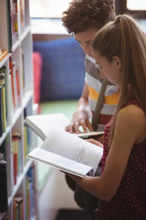 Attentive classmates reading book in library at school