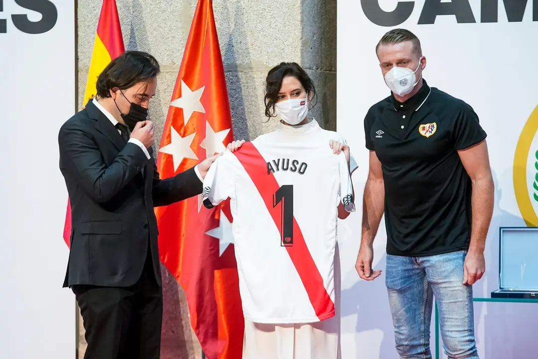 La presidenta de la Comunidad de Madrid, Isabel D&iacute;az Ayuso, posa con una camiseta de f&uacute;tbol con su nombre y con el presidente del Rayo Vallecano, Ra&uacute;l Mart&iacute;n Presa, y el capit&aacute;n Alberto Garc&iacute;a