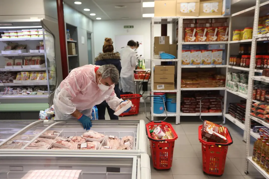 Archivo - Un voluntario manipula los alimentos de un refrigerador en el interior del economato solidario de C&aacute;ritas en Madrid.