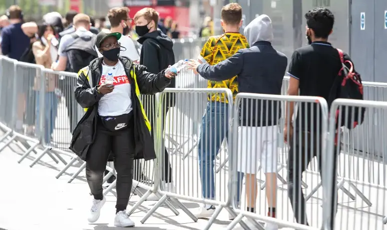 El personal reparte botellas de agua mientras la gente hace cola en un centro de vacunaci&oacute;n masiva contra el coronavirus en el estadio Emirates del Arsenal, en el norte de Londres. Fotograf&iacute;a: Dominic Lipinski/PA