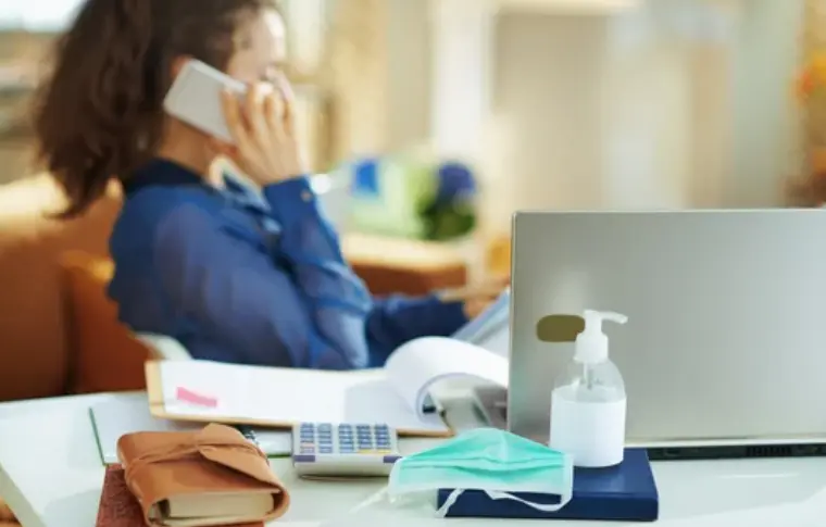 Una persona llama por tel&eacute;fono y en la mesa hay una mascarilla.