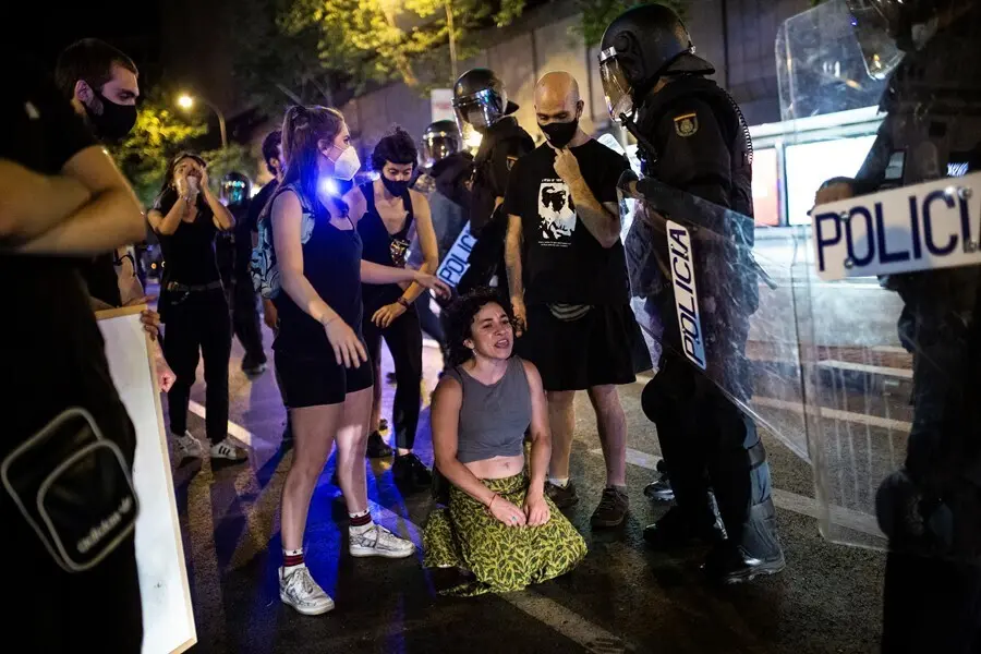 Una joven arrodillada frente a antidisturbios de la Polic&iacute;a Nacional en el barrio de Arg&uuml;elles tras la concentraci&oacute;n por el asesinato del joven Samuel a 5 de julio de 2021 en Madrid (Espa&ntilde;a). 