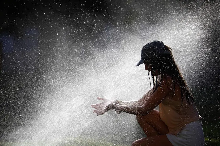 Una joven trata de mitigar los altas temperaturas que se alcanzar&aacute;n este domingo en C&oacute;rdoba, superiores a 40 grados, refresc&aacute;ndose con los aspersores de riego de un parque. EFE/Salas