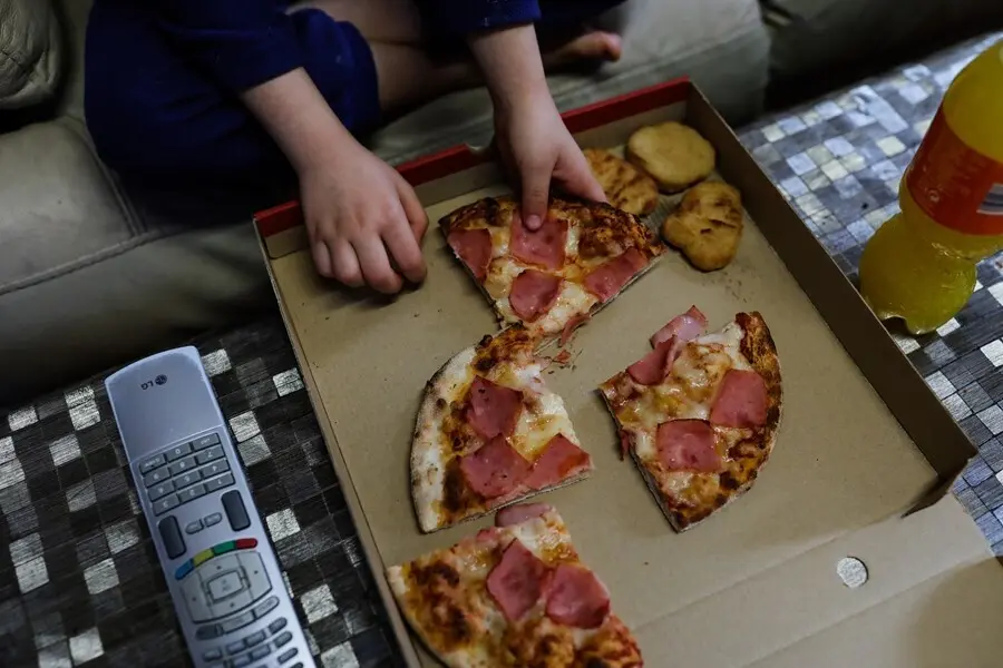 Archivo - Un ni&ntilde;o come pizza del men&uacute; infantil de Telepizza mientras ve la televisi&oacute;n en su casa