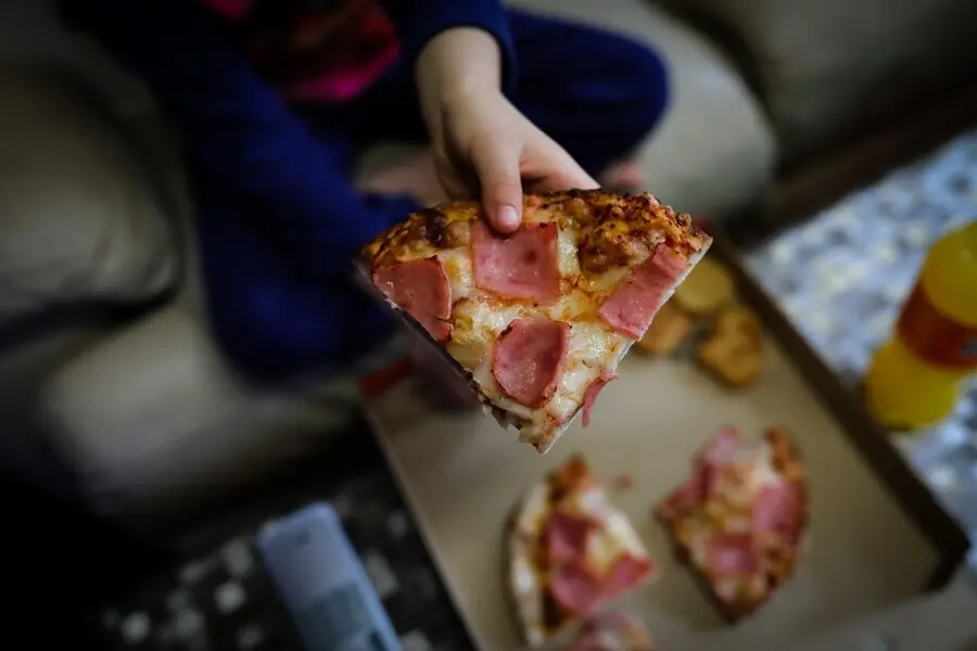 Archivo - Un ni&ntilde;o sostiene un trozo de pizza del men&uacute; infantil de Telepizza en el barrio de San Ferm&iacute;n en el distrito de Usera