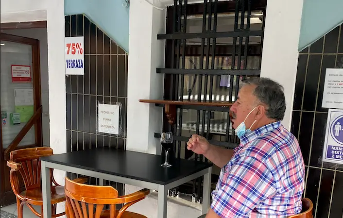 Un hombre toma un vino en una terraza en Santander bajo el cartel de 75% de aforno.  / ALERTA