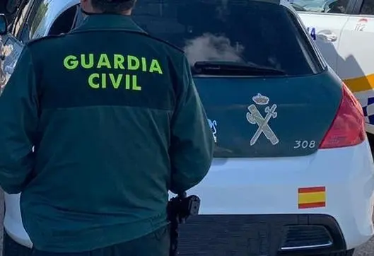 Archivo - Un agente de la Guardia Civil de espaldas y junto a un veh&iacute;culo oficial del cuerpo.