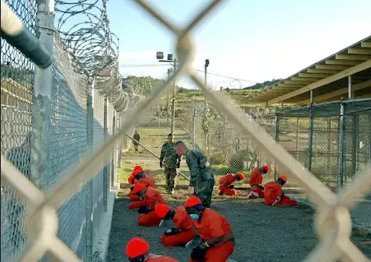 Detenidos sentados en una zona de detenci&oacute;n bajo la vigilancia de la polic&iacute;a militar estadounidense en Guant&aacute;namo en enero de 2002. Fotograf&iacute;a: Shane T Mccoy/AFP