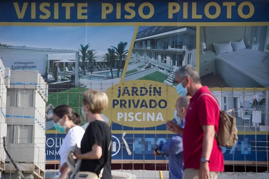Archivo - Varias personas caminan junto a un cartel de viviendas en venta 