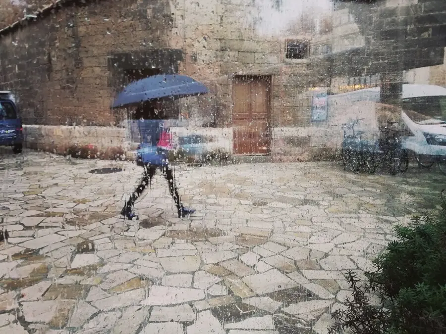 Archivo - Una mujer pasea por el centro de Palma con un paraguas, vista a trav&eacute;s de un cristal con gotas de lluvia.