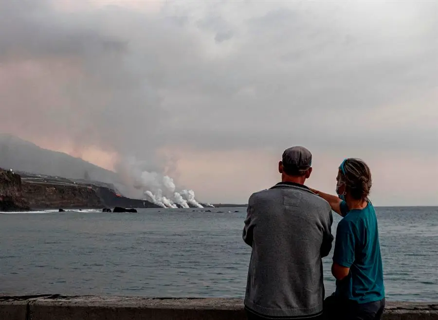 Unos turistas contemplan desde el puerto de Tazacorte la llegada al mar de la colada del volc&aacute;n Cumbre Vieja. EFE/MIGUEL CALERO