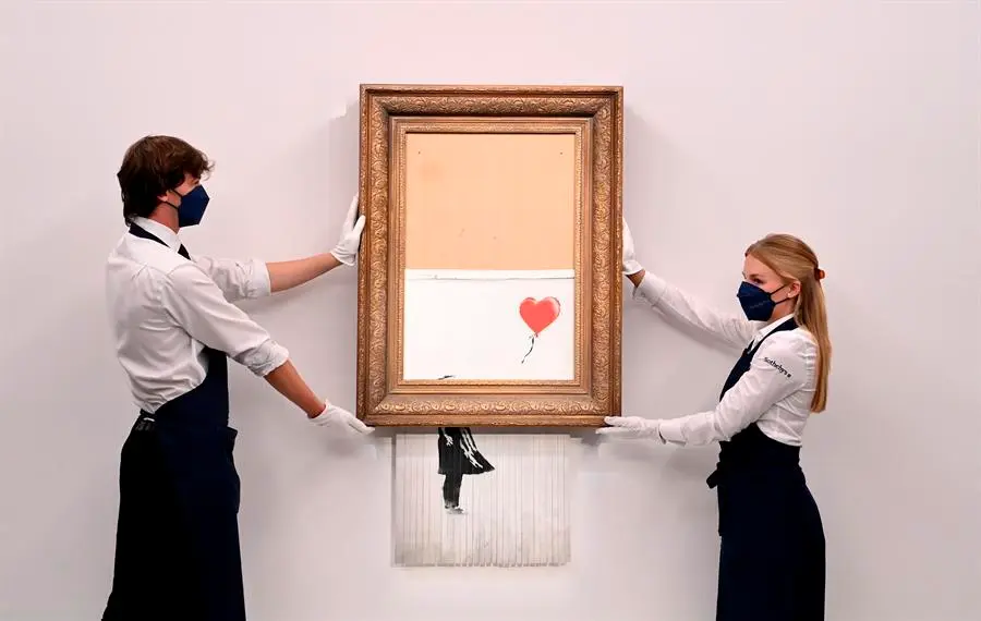 Empleados de la galer&iacute;a posan para los fot&oacute;grafos junto a un cuadro titulado "El amor est&aacute; en la papelera" del artista callejero brit&aacute;nico an&oacute;nimo Banksy en la casa de subastas Sotheby's en Londres, Gran Breta&ntilde;a 03 de septiembre de 2021