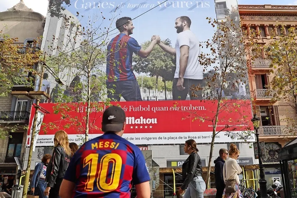 Un joven con la camiseta de Messi ante una pancarta de publicidad del cl&aacute;sico Bar&ccedil;a-Madrid, que se juega el domingo, ayer en las Ramblas de Barcelona. / Alejandro Garc&iacute;a