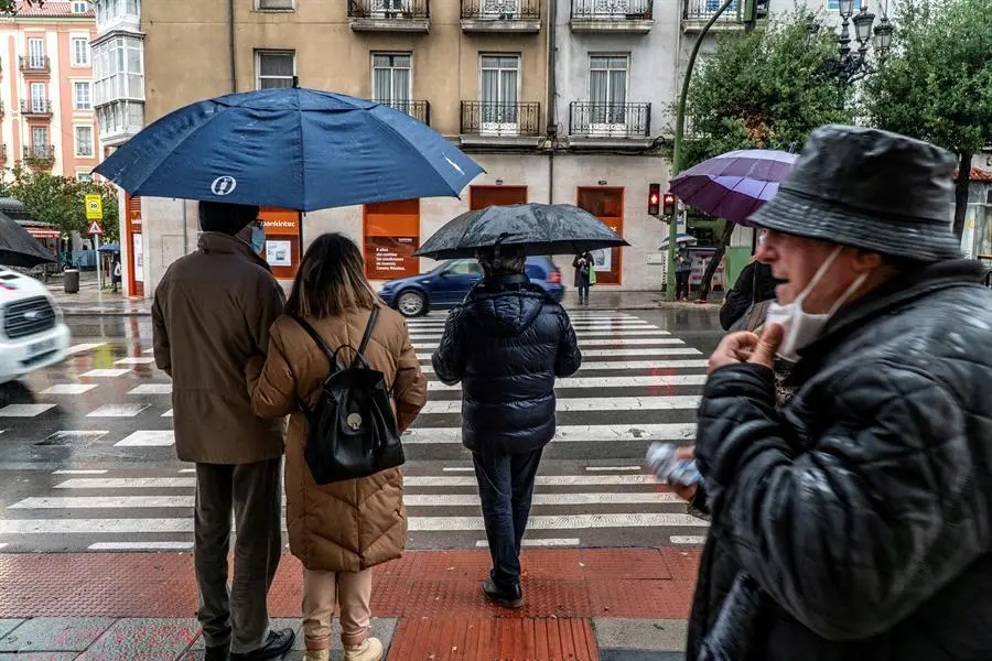 Varias personas con mascarilla y paraguas por la calle Casimiro Sainz de Santander. / EFE/Rom&aacute;n G. Aguilera