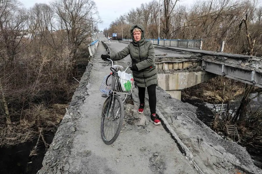 Una mujer pasa con su bicicleta por los restos del puente principal de la ciudad de Malyn, destruido tras el bombardeo de la aviaci&oacute;n rusa, en Malyn, Ucrania, el 12 de marzo de 2022. EFE/EPA/MIGUEL A. LOPES
