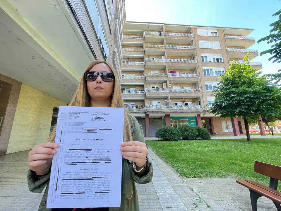 Elina en la plaza del barrio donde se ubica su vivienda, mostrando la sentencia que obliga a estas personas a salir de su casa. / alerta